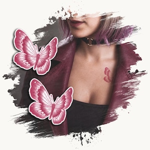 Puede incluir: Dos tatuajes temporales de mariposas rosas con patrones de alas detallados, junto a una persona que viste una chaqueta color granate oscuro, un top negro y un collar tipo gargantilla negro con un anillo dorado, con un pequeño tatuaje a juego.