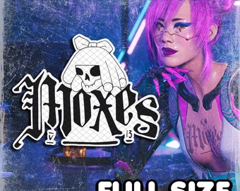 以下が含まれることがあります： 頭の上にリボンをつけた骸骨と「Foxes 13」というゴシック体で書かれた文字の入った一時的なタトゥー。タトゥーはピンクの髪とピンクと白の服を着た女性に施されている。