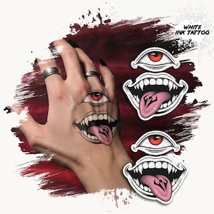 May include: A temporary tattoo design featuring a stylised eye with a red iris positioned above a wide, toothy mouth with a protruding tongue. The design includes the text WHITE INK TATTOO and is shown applied to a hand, with two additional sticker versions.