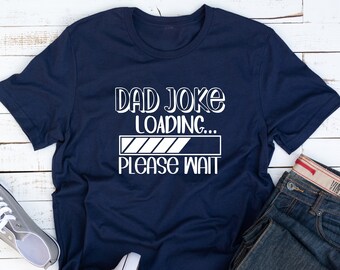 May include: A navy blue t-shirt with white text that reads "Dad Joke Loading... Please Wait". The text is in a stylized font and includes a progress bar graphic.