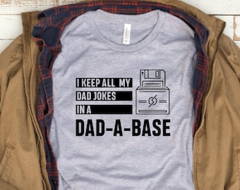 May include: A gray t-shirt with a black graphic of a floppy disk and the text "I keep all my dad jokes in a dad-a-base".