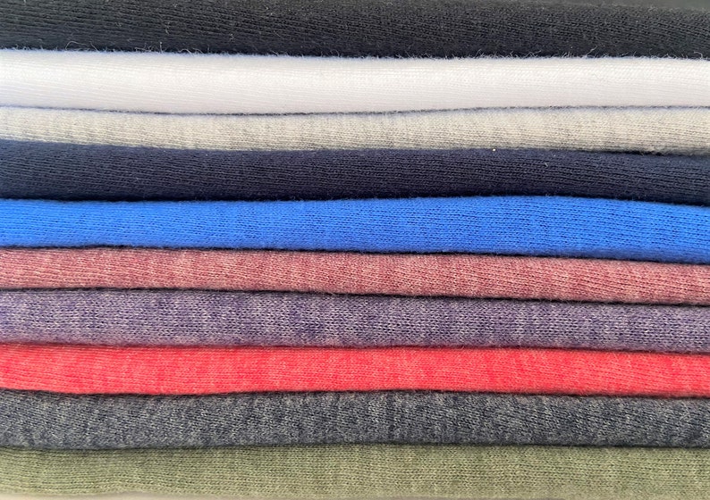 Pode incluir: Uma pilha de t-shirts dobradas em v&aacute;rias cores, incluindo preto, branco, cinza, azul, vermelho e verde.
