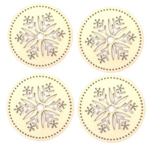 Pode incluir: Quatro bases para copos redondas de madeira clara com um desenho de floco de neve recortado no centro. Cada base para copos tem uma borda pontilhada. As bases para copos estão dispostas em uma formação quadrada.