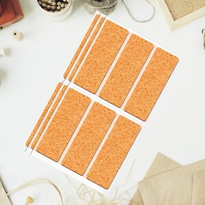 May include: A sheet of rectangular cork stickers with a natural, textured appearance. The stickers are arranged in rows and columns, with a white border around each individual sticker. The cork has a warm, orange-brown hue.