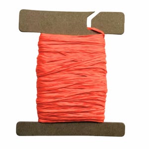 May include: A spool of vibrant coral-colored raffia ribbon. The raffia is tightly wound around a brown cardboard spool with a slot for hanging. The texture of the raffia appears slightly crinkled, adding visual interest to the craft supply.