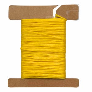 May include: A spool of bright yellow raffia ribbon wrapped around a rectangular brown cardboard holder. The ribbon has a textured, matte appearance and is wound horizontally across the center of the cardboard spool, which features notched edges.