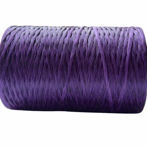 May include: A cylindrical spool of deep purple raffia twine. The material features a fibrous, textured appearance with visible strands wound tightly around the core, creating a consistent, uniform pattern across the entire surface of the spool.