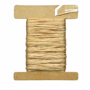 May include: A spool of natural-colored raffia ribbon. The raffia is tightly wound around a cardboard spool with a T-shaped design. The ribbon has a textured, slightly uneven appearance.