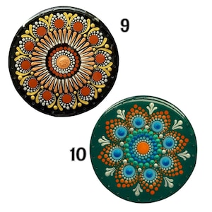 Pode incluir: Dois porta-copos circulares com mandalas em arte de pontos. O número 9 é preto com pontos laranja, amarelos e brancos. O número 10 é verde-escuro com pontos laranja, azuis e brancos. Ambos exibem padrões simétricos de círculos concêntricos.