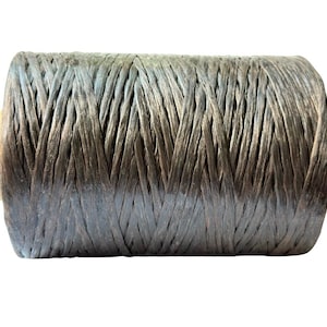 May include: A spool of gray-blue raffia ribbon. The ribbon is tightly wound around a cardboard core, creating a cylindrical shape. The raffia has a textured appearance, with visible fibers and a subtle sheen.