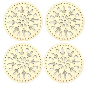 May include: Four round wooden coasters with a decorative floral cutout design. Each coaster has a series of small holes around the edge. The coasters are a light beige color.