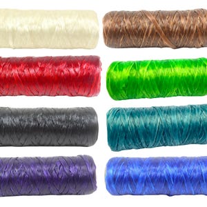 May include: Eight spools of raffia ribbon in various colors, including cream, brown, red, green, black, teal, purple, and blue. The raffia is tightly wound, showing a textured surface. Ideal for crafting and gift wrapping.