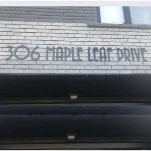 May include: A white brick building with a black metal awning. The building has a black metal sign that reads "306 Maple Leaf Drive".