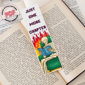 Pode incluir: Um marcador de página de ponto cruz com um esqueleto lendo um livro em uma cadeira com chamas atrás. O marcador de página tem o texto "Just One More Chapter" no topo.