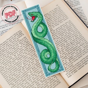 May include: A cross stitch pattern featuring a green snake with a red tongue, curled around a blue and white background. The pattern is framed with a blue border and includes the text "Cross Stitch Pattern PDF Instant Download".