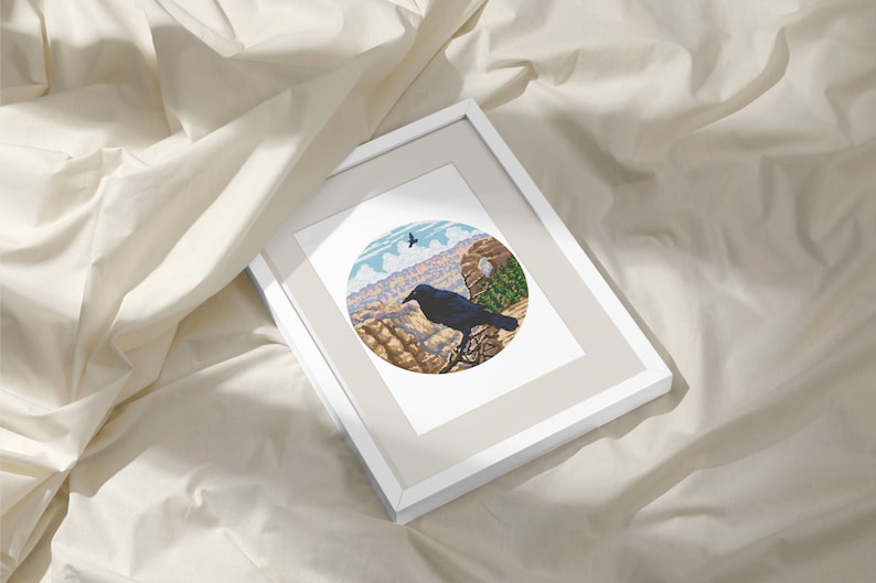 May include: A framed print of a black raven perched on a cliff overlooking a canyon. The raven is in the foreground, with the canyon in the background. The print is in a white frame with a beige mat.