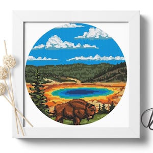 May include: A round cross-stitch pattern featuring a brown bison standing in front of a blue lake and a colorful landscape. The lake is surrounded by a yellow, orange, and red landscape. The background features a blue sky with white clouds.
