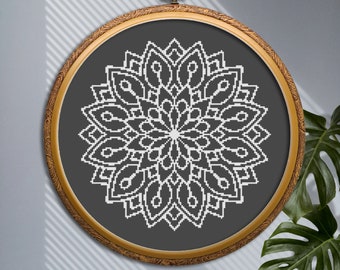 May include: A white mandala cross-stitch design on a dark gray background, framed in a round, ornate wooden hoop. The hoop is suspended by a brass-colored metal loop. The design is centered and features a symmetrical floral pattern.