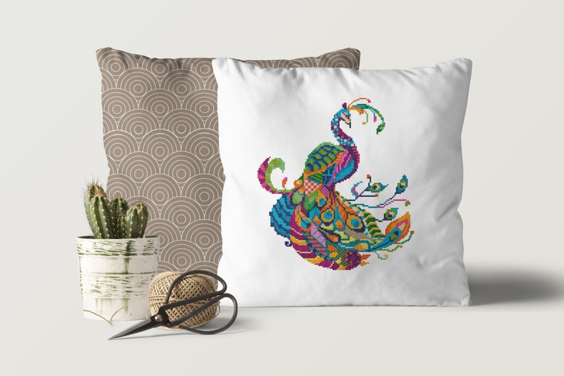 May include: A white cushion featuring an embroidered peacock design. The peacock is depicted in a stylised, geometric pattern with vibrant colours, including blue, green, yellow, orange, pink, and purple.