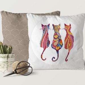 Pode incluir: Tr&ecirc;s gatos coloridos e com padr&otilde;es s&atilde;o representados em um design circular em uma almofada branca. Os gatos est&atilde;o de costas para o espectador, com suas caudas enroladas ao redor de seus corpos. A almofada &eacute; um acento decorativo para uma casa.