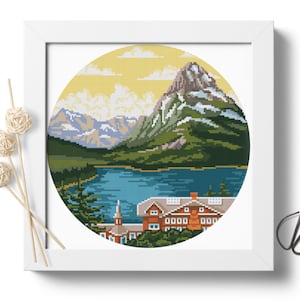 May include: A cross-stitch pattern of a mountain lake scene with a lodge in the foreground. The lake is blue, the mountains are green and brown, and the sky is yellow with white clouds.