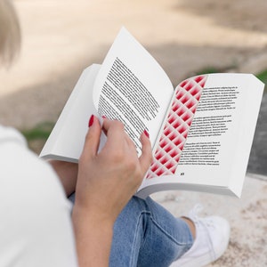 以下が含まれることがあります： 赤い白のしおりが付いた本を読んでいる人。本はテキストのあるページを開いています。その人は青いジーンズと白いシャツを着ています。