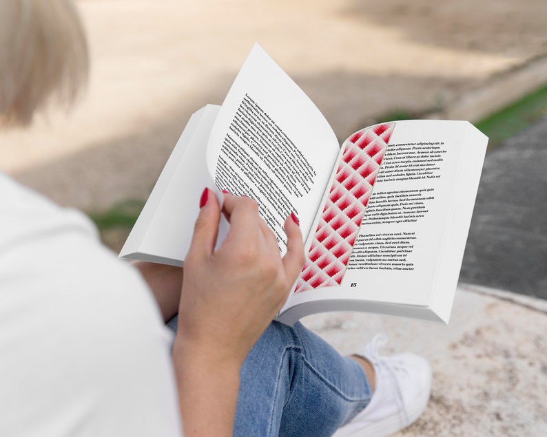 以下が含まれることがあります： 赤い白のしおりが付いた本を読んでいる人。本はテキストのあるページを開いています。その人は青いジーンズと白いシャツを着ています。