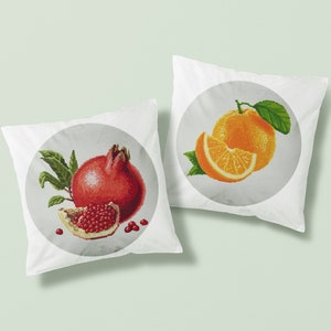 May include: Two white pillowcases with embroidered fruit designs. One pillowcase features a red pomegranate with green leaves and a slice of pomegranate. The other pillowcase features a whole orange and a slice of orange with green leaves.
