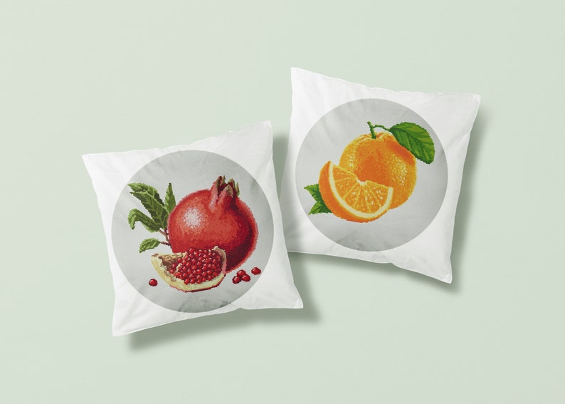 May include: Two white pillowcases with embroidered fruit designs. One pillowcase features a red pomegranate with green leaves and a slice of pomegranate. The other pillowcase features a whole orange and a slice of orange with green leaves.