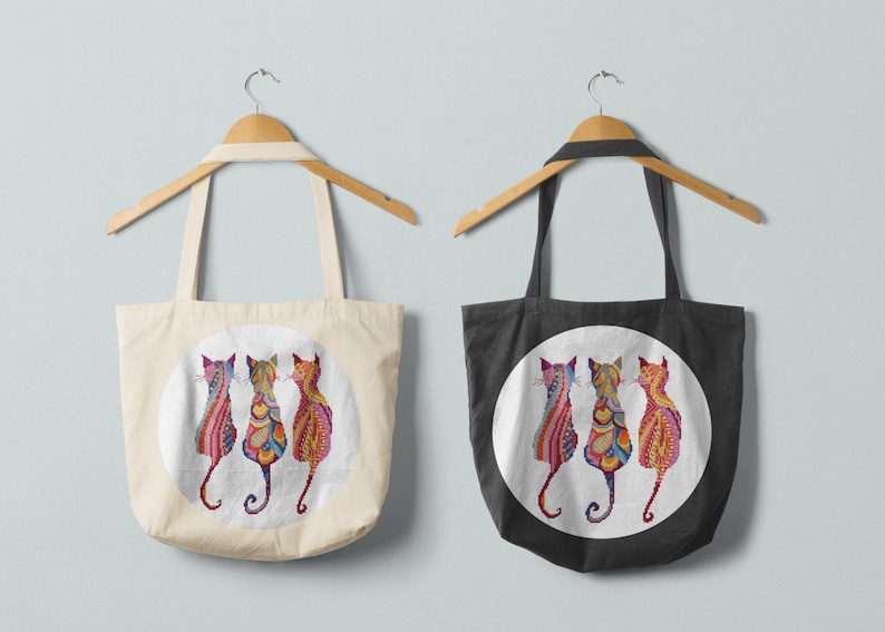 Pode incluir: Duas sacolas de compras com um design circular apresentando tr&ecirc;s gatos coloridos. A sacola &agrave; esquerda &eacute; branca e a sacola &agrave; direita &eacute; preta.