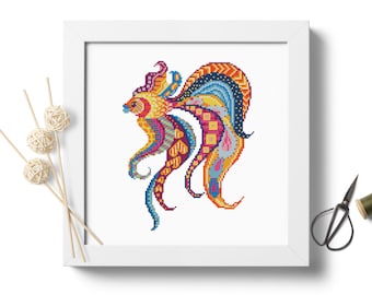 May include: A colorful cross-stitch pattern of a stylized fish with a yellow body and blue, red, and purple fins. The fish is framed in a white frame.
