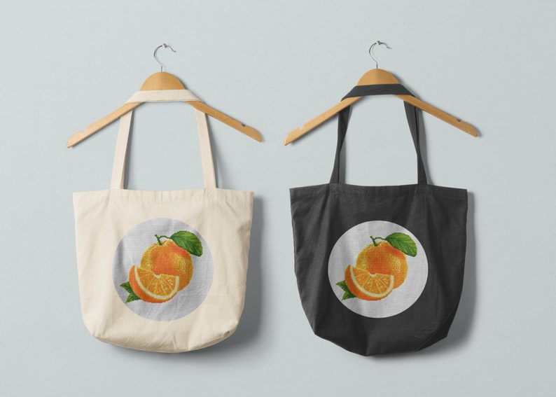 May include: Two tote bags with orange fruit designs. The bag on the left is white with a circle design featuring a whole orange and a slice of orange. The bag on the right is black with a circle design featuring a whole orange and a slice of orange.