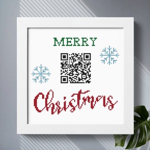 May include: A white framed print with the words "Merry Christmas" in red and green lettering. A black and white QR code is in the centre of the print with two blue snowflakes on either side.