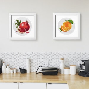 May include: Two framed illustrations of fruit. The left frame shows a red pomegranate with a slice of pomegranate. The right frame shows a whole orange with a slice of orange.