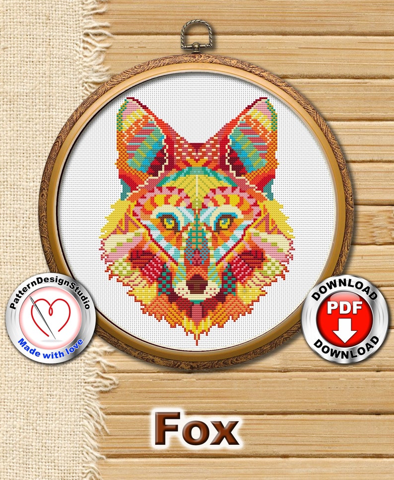 May include: A colourful cross-stitch pattern of a fox's head in a wooden embroidery hoop. The fox is depicted in a geometric style with vibrant colours, including red, orange, yellow, green, blue, and purple. The pattern is framed by a wooden hoop with a gold finish. The words "Pattern Design Studio" and "Made with love" are printed on a red heart-shaped label below the hoop. The words "Download PDF" are printed on a red circle with a downward arrow.
