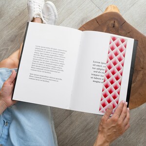 以下が含まれることがあります： ピンクと白のしおりが付いた本を読んでいる人。しおりは幾何学模様です。