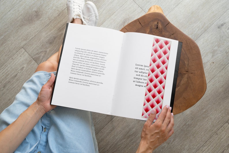 以下が含まれることがあります： ピンクと白のしおりが付いた本を読んでいる人。しおりは幾何学模様です。