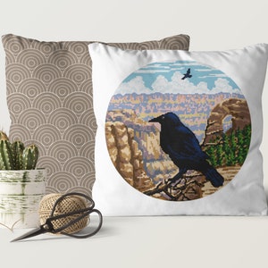 May include: A white pillow with a round, colorful image of a canyon landscape and a black raven perched on a branch. The raven is looking to the left. The image is surrounded by a white circle.