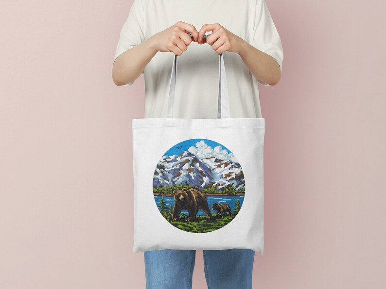Pu&ograve; includere: Borsa tote in tela bianca con un design circolare che presenta un orso bruno e un cucciolo che camminano in un paesaggio montano con un lago blu e un cielo blu con nuvole bianche.