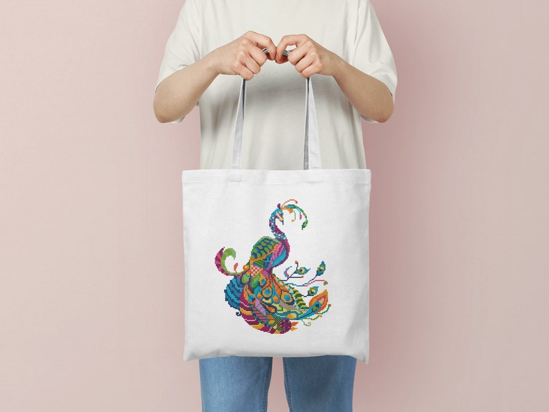 May include: A white tote bag featuring a colourful peacock design printed on the front. The peacock is made up of various geometric shapes and patterns.