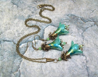 Può includere: Un set di gioielli con collana e orecchini a tema floreale. I ciondoli a forma di fiore blu turchese hanno dettagli dorati e perline verdi. La catena e i ganci degli orecchini sono color bronzo.