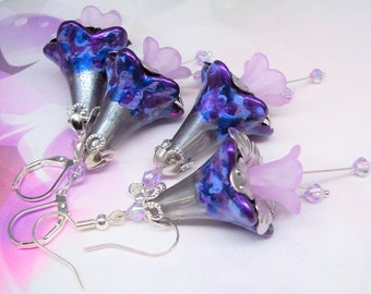 May include: Earrings featuring bell-shaped flowers with a metallic silver base and vibrant purple and blue marbled accents. Each earring has a delicate lavender flower and sparkling crystal accents, with silver-tone lever-back closures.