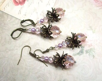 May include: Three pairs of dangle earrings with a vintage aesthetic. Each earring features a large, faceted pink crystal bead, surrounded by a dark bronze-colored filigree flower. Smaller pink and purple beads accent the design, with bronze ear wires.