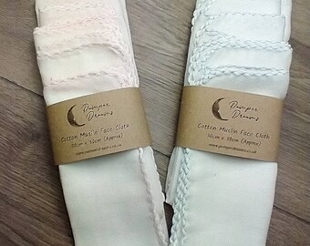 May include: Two stacks of white cotton muslin face cloths, each wrapped with a brown paper band. The cloths are approximately 12 inches by 12 inches, with a decorative stitched edge. The paper band reads "Pamper Dreams" and "Cotton Muslin Face Cloth".