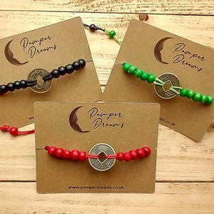 May include: Three bracelets with brown card backing. Each bracelet has a different color of beads: black, green, and red. Each bracelet has a round, silver-colored coin charm with Chinese characters.