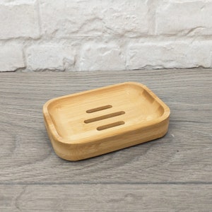 May include: A rectangular wooden soap dish with three drainage slots. The dish is made of light brown bamboo.