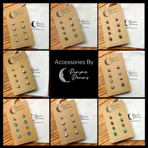 May include: Six sets of earrings on brown cards with the text "Pamper Dreams" on each card. Each set includes three pairs of earrings with different shapes and colors.