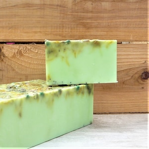 May include: Two rectangular bars of handmade soap. The soap is a light green colour with darker green and brown accents on the top. The bars are stacked, with a wooden background.
