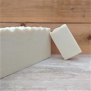 May include: Two bars of white soap, one lying flat and the other leaning against a wooden surface.