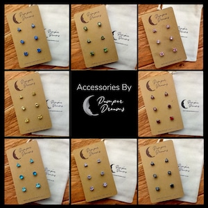 May include: Nine sets of small, colourful stud earrings displayed on brown cards with a moon and star logo. Each set includes three earrings in different shapes and colours. The cards are labelled "Pamper Dreams".